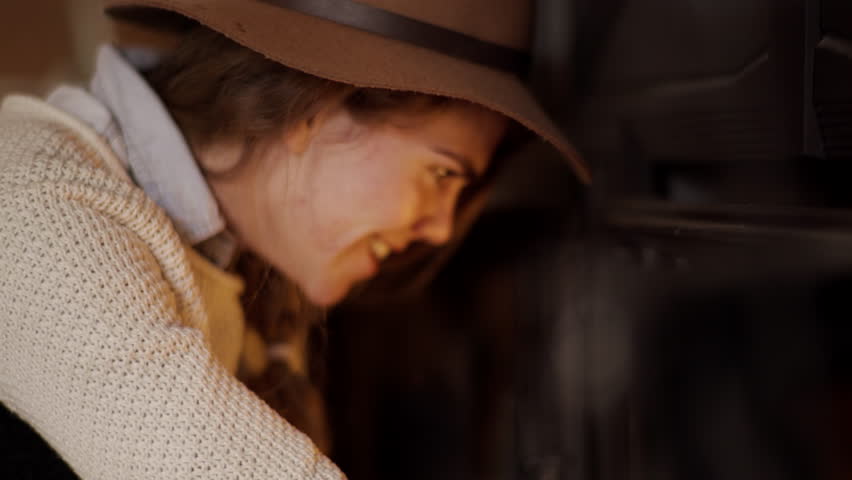 Young Woman Chats With Someone Off-Screen And Stokes Fire, Blows On Flame 