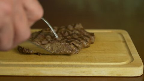 Hand salt steak. The salt slowly falls on top of the meat. The meat lies on a wooden board.