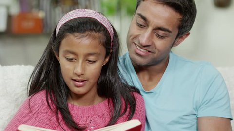 Father and daughter of Indian ethnicity spending time together at home, reading a book Arkistovideo
