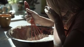 Young girl playing with flour while preparing dough with whisk in metal bowl
