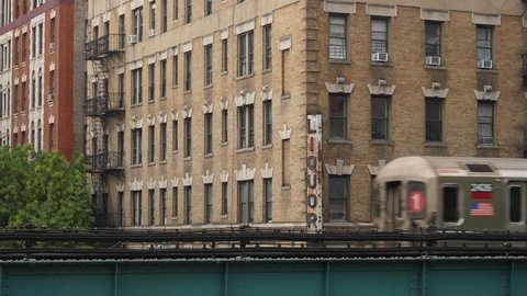 A New York City subway train passes by Harlem apartment buildings and a corner liquor store on an elevated track. Shot at 60fps for optional slow motion.  	