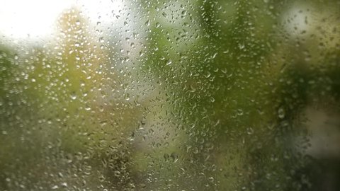 Raindrop on window glass with blurry tree background. Closeup wideangle shot.