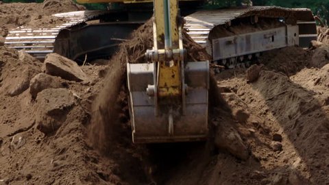 Excavator bucket digging through dirt and rocks at a construction site in slow motion.