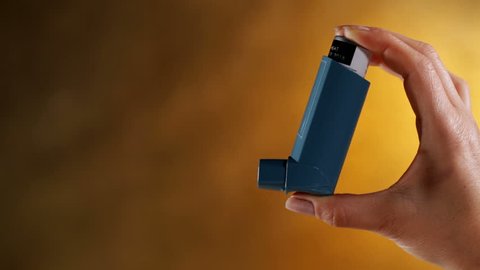 Woman hand sprays three puffs from vapor inhaler device - closeup