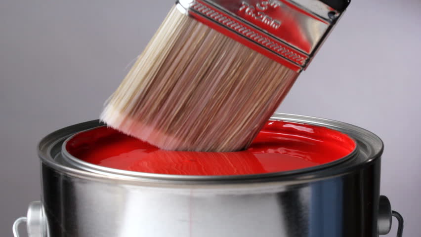 Paint brush dips into can of red paint
