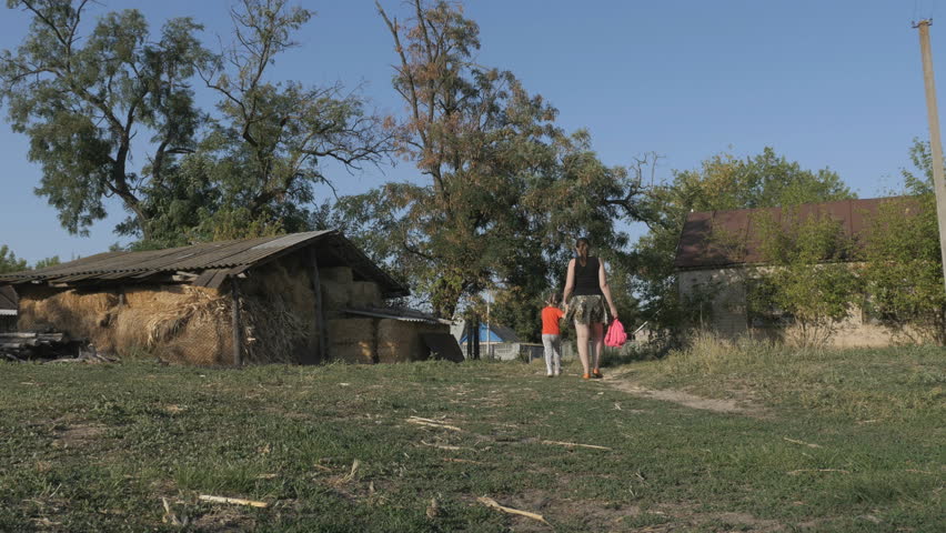 Countryside. Mother and daughter going along the path near hay bales, stacks and agricultural warehouses
