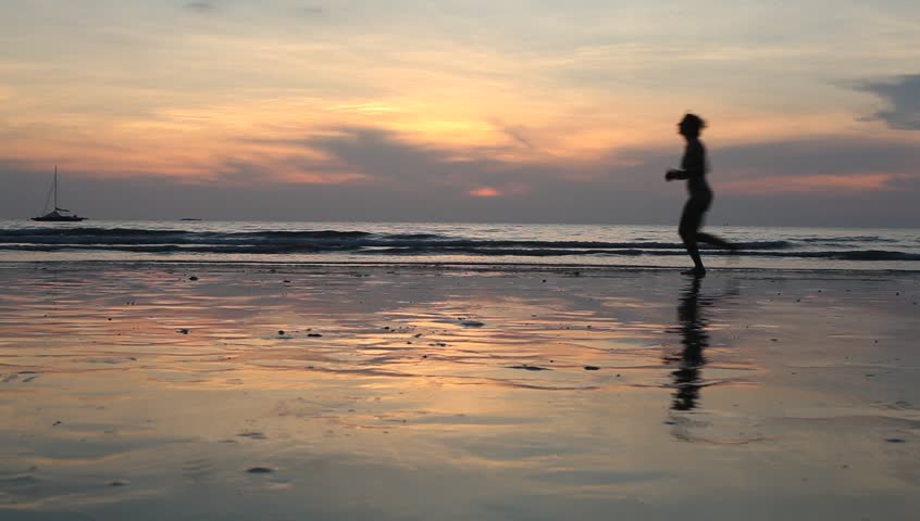 Silhouette of woman jogging on the beach after a sunset