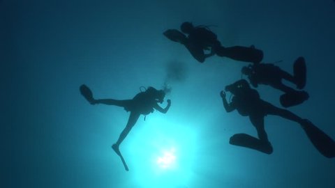 scuba divers coming up surface underwater with sun beams and rays