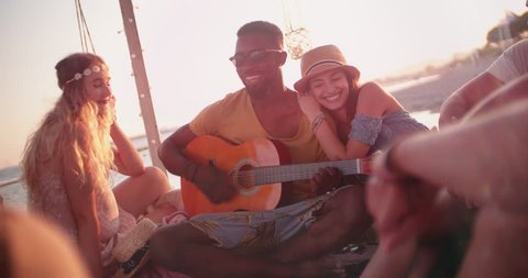 Multi-ethnic hipster friends and couples playing the guitar and having fun at summer beach bar