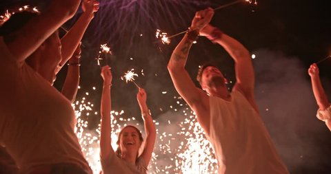 Multi-ethnic friends with arms outstretched celebrating fourth of July with sparklers, confetti and fireworks display
