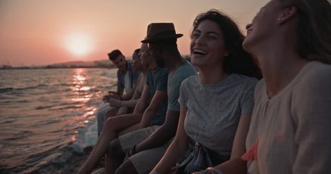 Young multi-ethnic hipster friends on summer holidays relaxing and having fun on pier at sunset