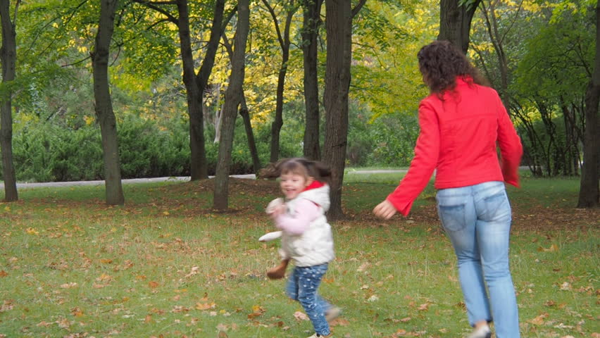 Happy family playing in the park. Mother and daughter are running around in the autumn park.