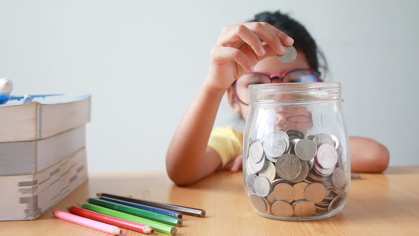 Asian little girl putting the coin into a  clear glass jar with the book on table metaphor saving money for education concept | Shutterstock HD Video #31791229