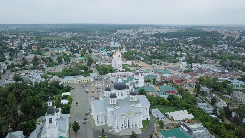View of the Resurrection Cathedral from above. The five-domed neoclassical cathedral with its columned portico and dark cupolas dominates Cathedral Square in Arzamas, Russia, surrounded by a dense historic cityscape of low-rise buildings, green trees, and converging streets. Built to commemorate Russia