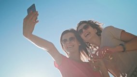 Two young ladies making a selfie on the beach. Medium shot. Soft Focus.