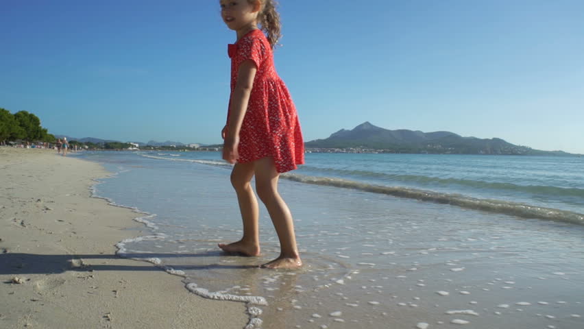 Little girl in bright red dress running on the beach barefoot