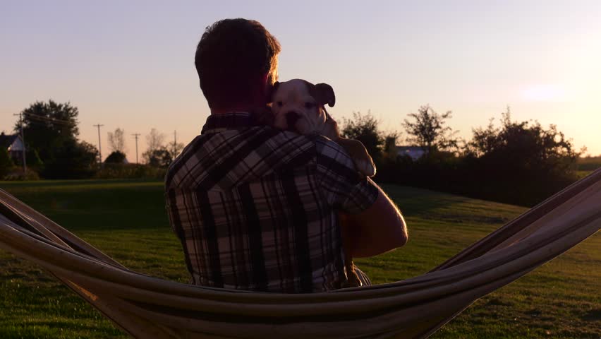 guy and his puppy bulldog in hammock hugging in sunset