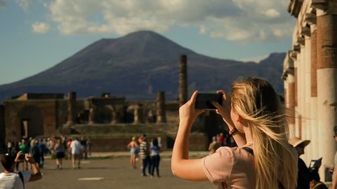 Pompeii Ruins, Italy Tourism. UNESCO World Heritage Site. Young Woman Exploring Europe.Tourist Woman Exploring Pompeii While Traveling In Italy. Woman Tourist Taking Photograph. Volcano Vesuvius