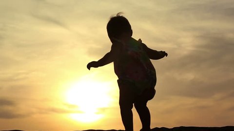 Silhouette of adorable baby girl walking over sunset