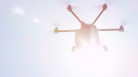 CLOSE UP LENS FLARE: UAV drone delivery. Multicopter flying brown package over sun. Drone delivering goods to your home. Futuristic shipment by helicopter drone. Multirotor logistics and transport