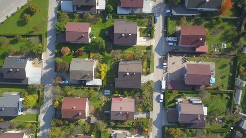 AERIAL TOP DOWN Flying over red rooftops in idyllic suburban town on sunny autumn day. Row houses with green garden lawns and narrow empty roads in peaceful suburbia. Perfect homes in quiet suburbia