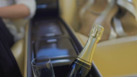 Champagne bottle and glass in inside car storage box, woman sitting at back seat