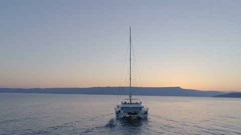 Aerial Shot of a Sailing Yacht with Sailes Down Moving on a Calm Sea Towards Clear Evening Horizon. Shot on Phantom 4K UHD Camera.