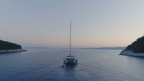 Tranquil Aerial Shot of a Catamaran Yacht Sailing out of the Beautiful Bay. It's Evening Sky is with a Tint of Pink and Tropical Coasts Visible. Shot on Phantom 4K UHD Camera.