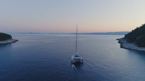 Tranquil Aerial Shot of a Catamaran Yacht Sailing out of the Beautiful Bay. It's Evening Sky is with a Tint of Pink and Tropical Coasts Visible.Shot on Phantom 4K UHD Camera.