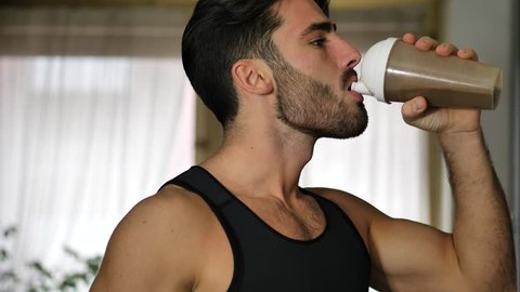 Young athletic man drinking a healthy smoothie drink or a protein shake from blender or shaker at home in kitchen