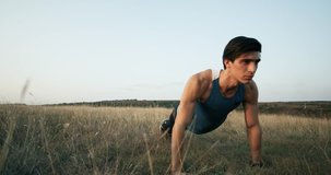 A handsome man in trendy outfit makes push ups during the video. He is wearing a blue T-shirt . The male is working out in the park. Slow Motion. 4k