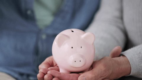 family, savings, old age and people concept - smiling senior couple putting money into piggy bank