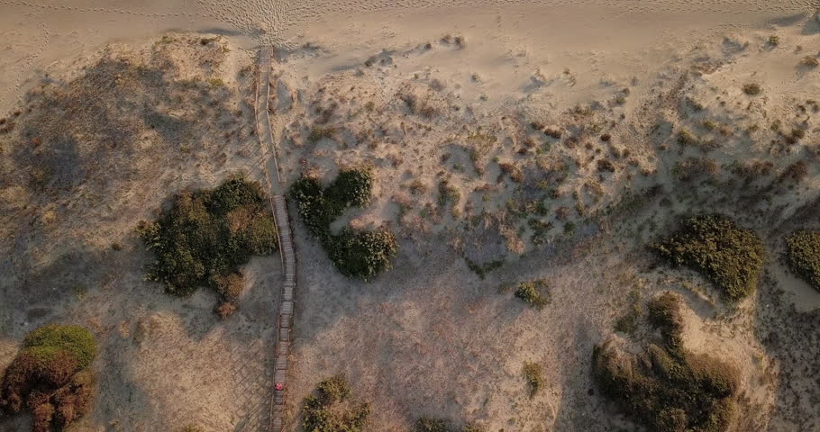 Video from above. Aerial view of a person walking along a boardwalk that leading to the Beach at sunset.	
