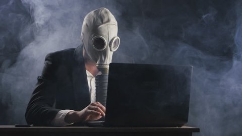 Businessman wearing gas mask working at laptop in dark office