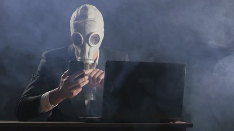 Businessman wearing gas mask working at smartphone in dark office