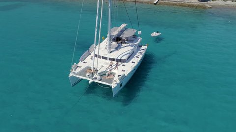 Aerial View of a Anchored Catamaran Yacht Standing with People Sunbathing on it's Deck. Boat Stands in Azure Sea Waters With Coral Reef Visible.Shot on Phantom 4K UHD Camera.