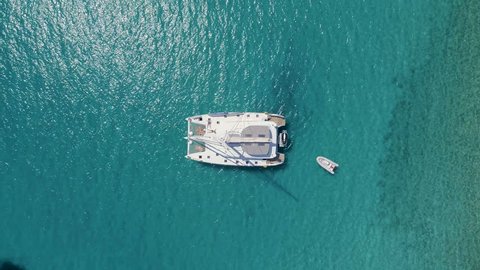 Aerial Top Down View of a Anchored Catamaran Yacht with People Sunbathing on it's Deck. Boat Stands in Azure Sea Waters With Coral Reef Visible.Shot on Phantom 4K UHD Camera.