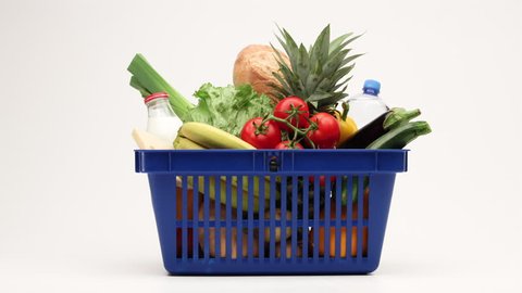 Side view on shopping basket filled with vegetables, bread and milk products moving on white background. 4K stop motion animation.