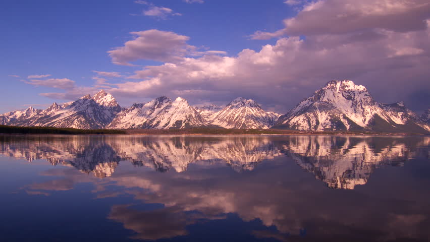 Grand Teton National Park - snow-capped mountain peaks at sunrise with dramatic lighting and cloud formations. Reflections in water.