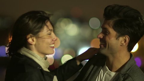 An attractive couple in love embrace and enjoy an intimate moment together, against the backdrop of city lights: film stockowy