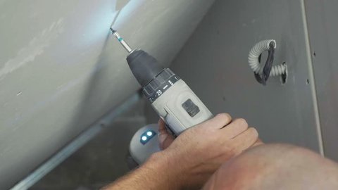 Worker make install drywall and using screwdriver and screw for work at newly built house. Close-up hands shots.