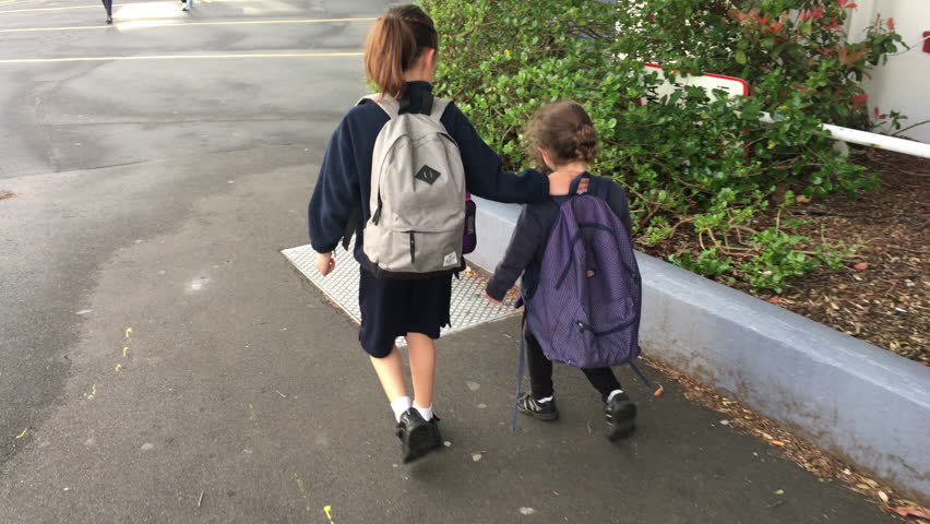 Two young sister girls (age 07 and 03) walking in the street together to school. 