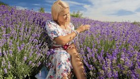 Slow motion video of beautiful blonde girl sitting in the middle of lavender field at sunny day