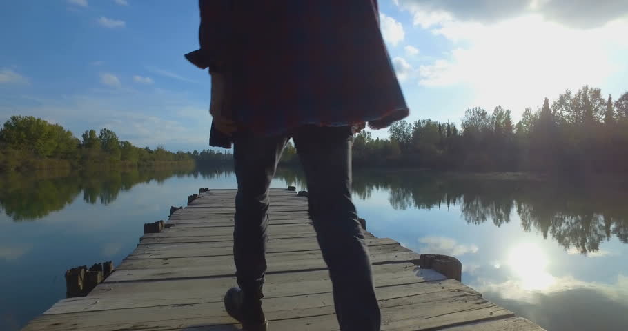 Boy with black boots shoes and particular circular hat  is walking on the Jetty near the Lake.