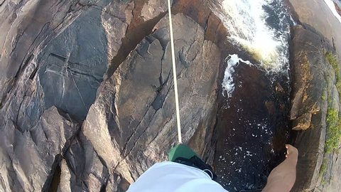 Point of view shot of a man walking across a rope, slacklining, between two cliffs over a dangerous river in Asia during the day