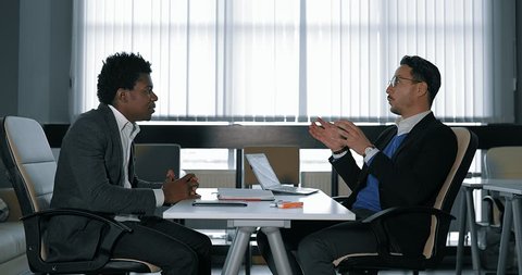 two young businessman talking at desk in office. shake hands with each other. European and African businessmen