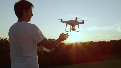 SLOW MOTION CLOSE UP LENS FLARE Young man hand launching quadro drone with modern white RC transmitter. Male filmer controlling drone over RC radio controller. Man flying and filming with drone camera