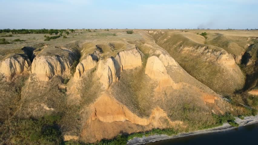 An impressive bird`s eye view of high clay hills covered with sagebrush. The picturesque seascape with a nice sunset looks gorgeous. The narrow seashore is covered with sand