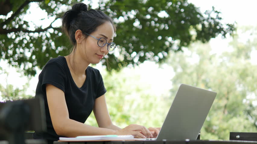4K: Asian woman working on modern laptop in the park.