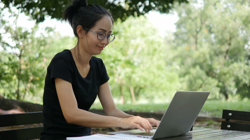 4K: Asian woman working on modern laptop in the park.